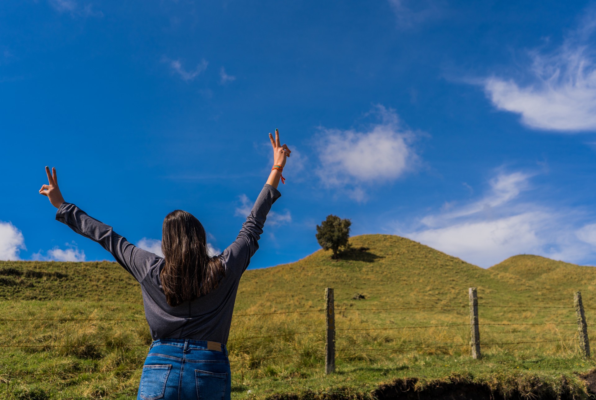 young woman at the edge of a mountain with her back turned and her arms open wide